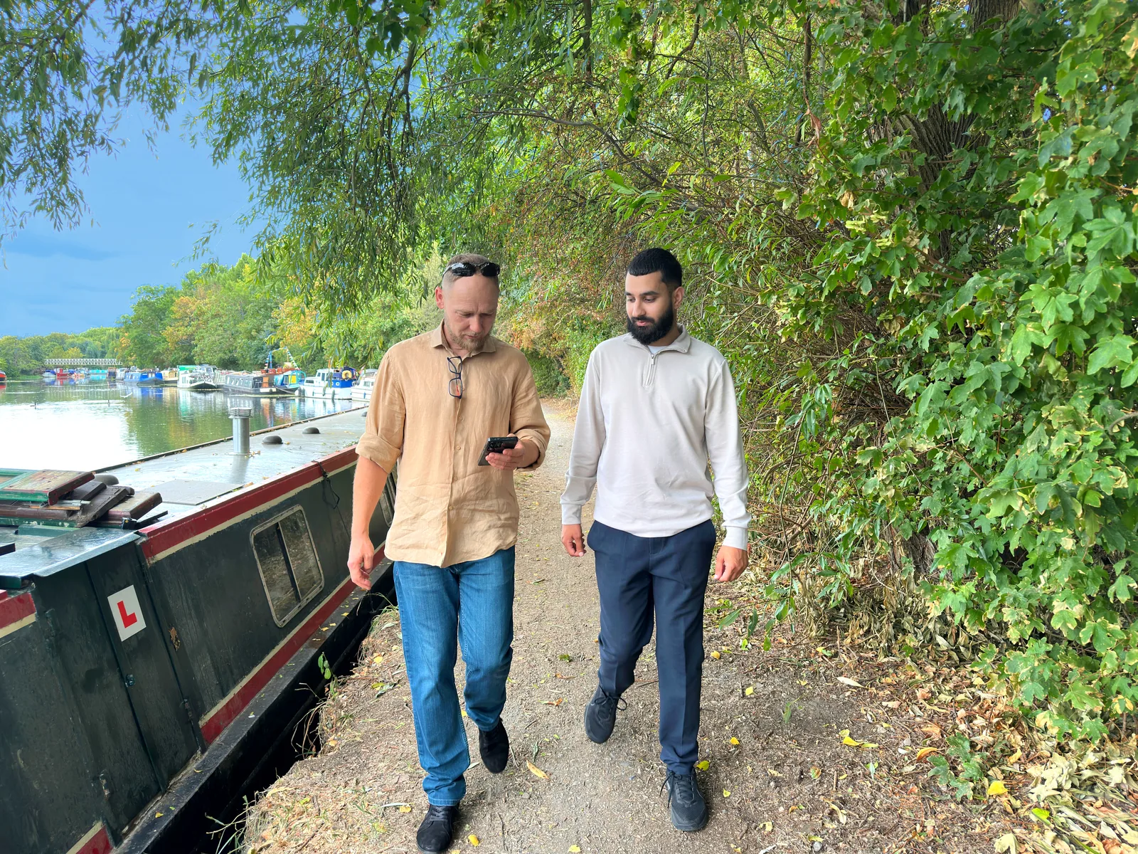 Two men walking along a tree-lined canal towpath.