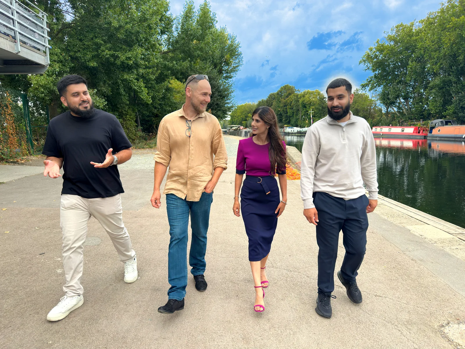 Four people walking beside moored canal boats.