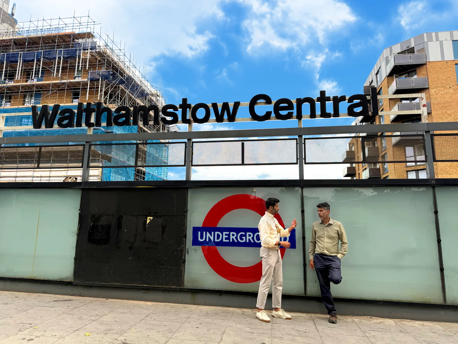 Two men talking beneath the Walthamstow Central station sign.